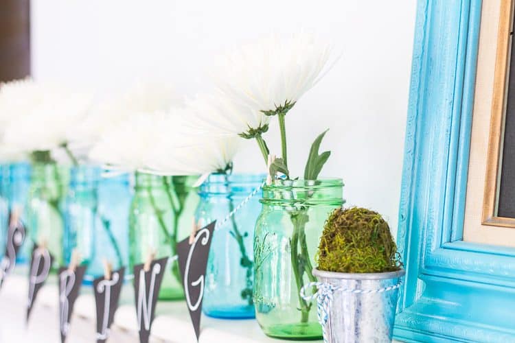 Chalkboard Spring Mantel with blue and green mason jars and white daisies.  A simple Spring Mantel full of color with touches of green moss and galvanized buckets.