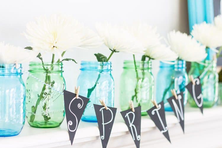Chalkboard Spring Mantel with blue and green mason jars and white daisies.  A simple Spring Mantel full of color with touches of green moss and galvanized buckets.