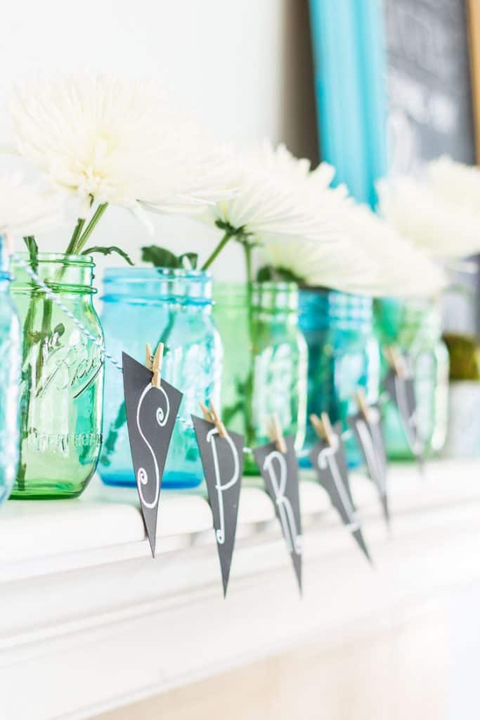 Chalkboard Spring Mantel with blue and green mason jars and white daisies.  A simple Spring Mantel full of color with touches of green moss and galvanized buckets.