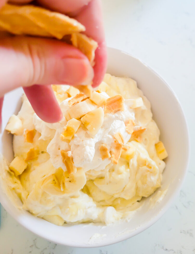adding crumbled waffle cookies to the top of banana pie dip
