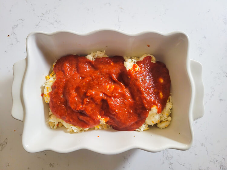 adding pizza sauce to top of cheese mixture